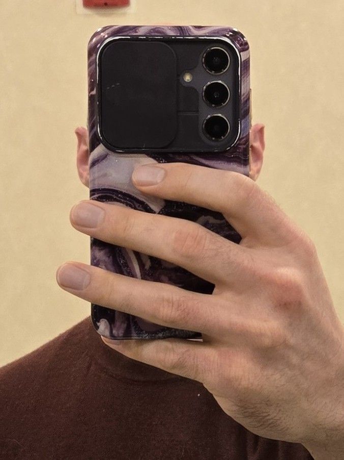 A caucasian male in a red sweater. Except for his ears, his head is completely obscured by the phone he's holding up to the mirror.
