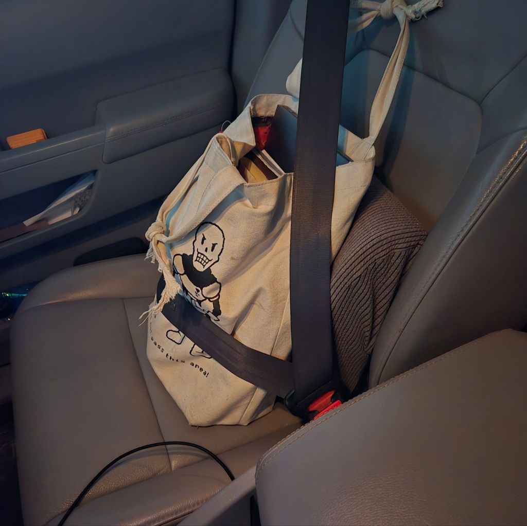 A tote bag containing a laptop and various papers, safely buckled into the front passenger seat of a car. 
